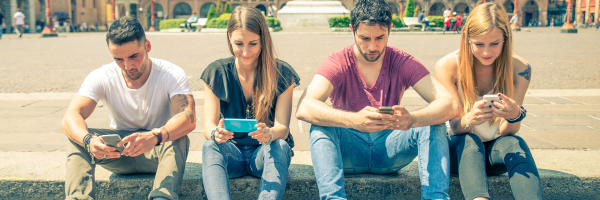 Vier jongeren zitten aan de rand van een plein op hun mobiele telefoon.